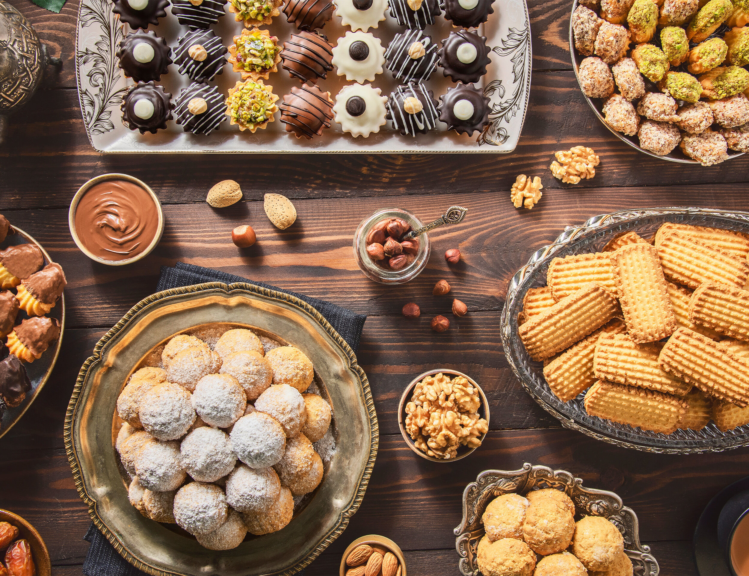Assorted Eid desserts including cookies, baklava, chocolate treats, and nuts arranged on a wooden table.